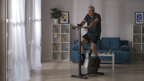 healthy-middle-aged-man-is-training-on-stationary-bike-in-home-general-shot-in-living-room-fitness-and-healthy-lifestyle-keeping-fit